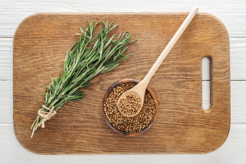 top view of rosemary and coriander in bowl with wooden spoon on chopping board
