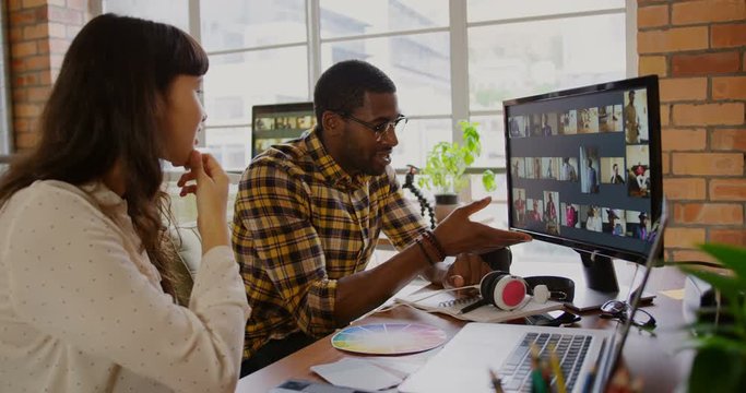 Graphic designers working on photos over computer at desk in office 4k