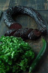 Blood sausage on a dark cutting board decorated with curly parsley. Blood sausage. View from above. Dark wooden background.
