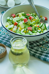 Salad with corn, crab sticks, cucumbers in a white bowl on a white background. Vegetarian salad. Cooking process.