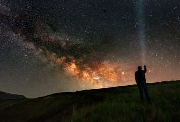 Naklejka na ściany i meble Beautiful starry night, man silhouette stands on in the hill and looks at the Milky Way galaxy.