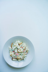 Salad with crackers, crab sticks, chicken fillet, fresh greens and hard cheese, seasoned with mayonnaise oil, served in a white plate. Salad with mayonnaise. White background. Space for text.