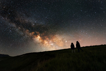 Beautiful starry night, two silhouette stands on in the hill and looks at the Milky Way galaxy.