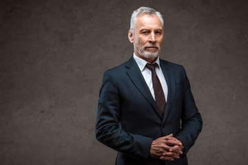 successful businessman in suit standing with clenched hands on grey