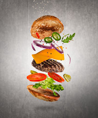 Tasty double cheeseburger with flying ingredients on dark background. High resolution image.