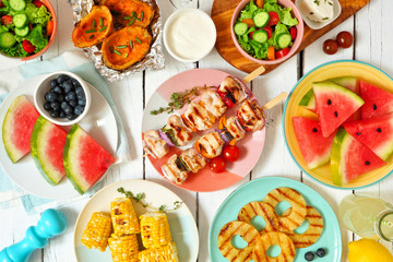 Summer BBQ or picnic food concept. Selection of fruits, salad, grilled meat and potatoes. Top view table scene over a white wood background.