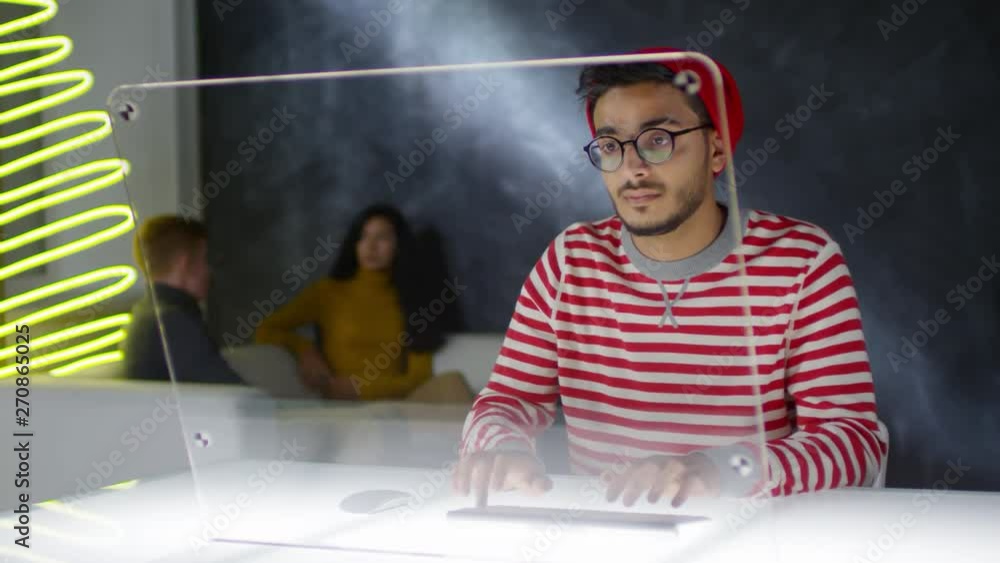 Aufkleber lockdown of young arab man sitting at see-through monitor of futuristic computer and typing on wirel