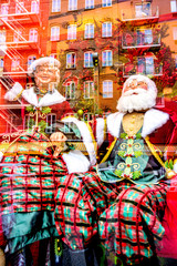 Santa Claus and Santa Clara on glass window reflection with bricks buildings background, Christmas gifts.