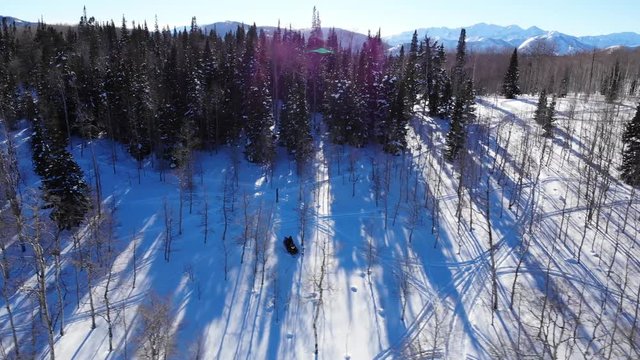 Panoramic aerial shot of Heber Valley mountains trees and snowscooters. This video shows mountains of Heber Valley on the horizon and trees with two snowmachines.