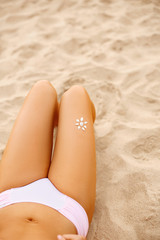 Young woman with sun shape on the leg holding sun cream bottle on the beach. Sun protection sun cream, on her smooth tanned legs. Sunblock. Skincare