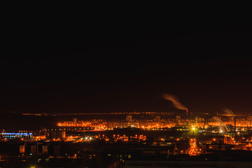Fototapeta na wymiar City downtown at night.City skyline in the dusk. Amazing panoramic view of modern city. Aerial view of residential flats of dormitory area close to industrial zone, factory pipes with smoke