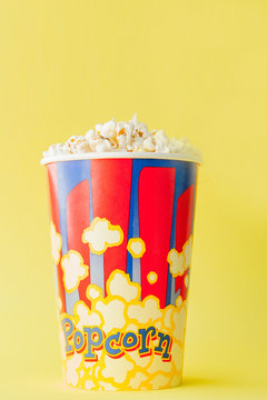 Popcorn in a red and white cardboard box on a yellow background. Copy space. Flat lay