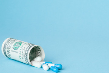 Money dollar rolled up with pills flowing out isolated on blue background, high costs of expensive medication concept. Copy space