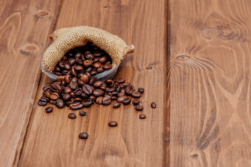 Fresh roasted coffee beans falling out the sack on the wooden surface. Brown coffee beans scattered from bag on the table