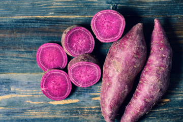 Purple sweet potatoes on wooden background, top view
