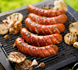 Grilled sausages with the addition of herbs and vegetables on the grill plate, outdoors. Grilling food, bbq, barbecue