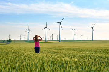 Woman and wind turbines at sunset, in a field of green rye, with warm sun light. Concept for...