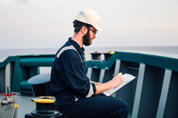 Deck Officer on deck of offshore vessel or ship , wearing PPE personal protective equipment. He fills checklist. Paperwork at sea