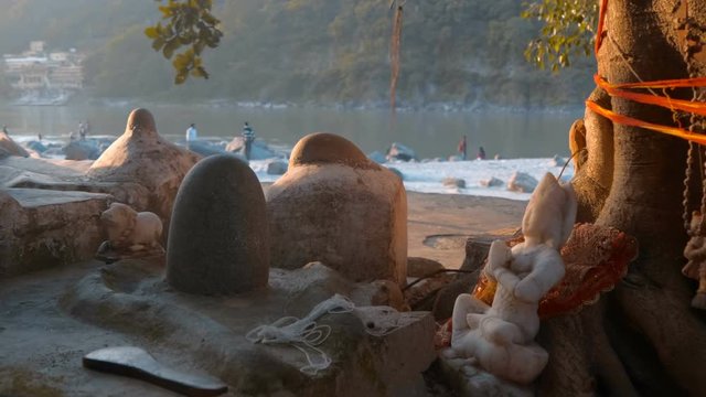 Stone figure of the Indian God on the banks of the sacred Ganges River in the light of sunset, in the city of Rishikesh, India, candles are burning and incense is smoked nearby. Shot in motion