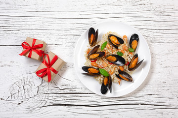 Fried rice with seafood mussels, shrimps and basil in a plate with gift boxes on white cracked wooden table