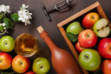 Ripe red and green apples in wooden box with branch of white flowers, glass and bottle of cider on a rusty background