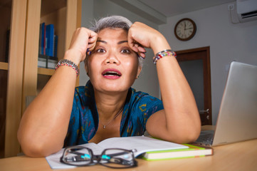 office lifestyle portrait of sad and depressed middle aged attractive Asian woman working on laptop...