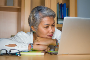 attractive depressed and sad mature Asian business woman working at office computer desk feeling...