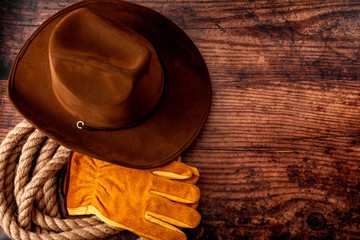 American culture, living on a ranch or farm and country muisc concept theme with a cowboy hat, rope lasso and rodeo leather gloves on a wooden background in a old saloon with copy space - obrazy, fototapety, plakaty