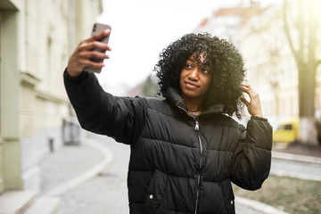 Cheerful young african woman taking a selfie wearing coat walking outdoors