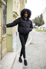 Cheerful young african woman wearing coat walking outdoors in the street