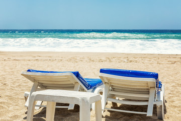 Sun beds on a sandy beach against the blue sea on a sunny windy day.
