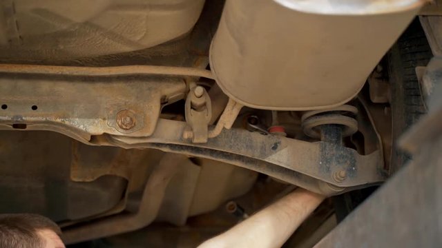 The master in the inspection pit in the service station adjusts the alignment of the car. Car lighter unscrews the nut on the car with a wrench.