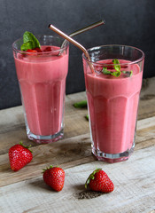 strawberry smoothie in a tall glass with metal straws. on a wooden table. with mint leaves.