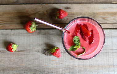 strawberry smoothie in a tall glass with metal straws. on a wooden table. with mint leaves.