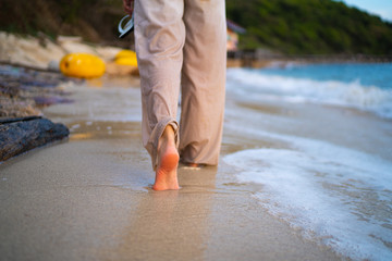 Closeup of a women's bare feet walking at a beach at sunset, with a wave's edge foaming gently...