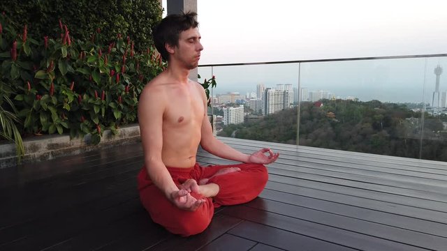  a man meditates sitting on a wooden, being on the observation deck on the background of the city. 
