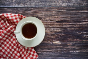 A cup of tea with a red weathered cloth over a wooden background, top view