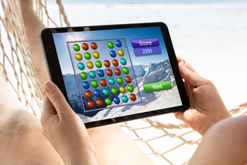Woman Lying On Hammock Playing Video Game On Digital Tablet