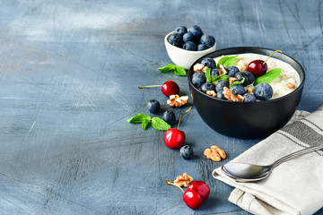 Oatmeal cereal porridge with fresh berries  in black bowl. Healthy breakfast. Top view on gray  table