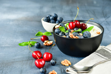 Oatmeal cereal porridge with fresh berries  in black bowl. Healthy breakfast. Top view on gray  table
