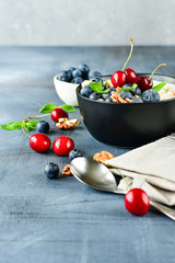 Oatmeal cereal porridge with fresh berries  in black bowl. Healthy breakfast. Top view on gray  table