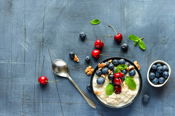 Oatmeal cereal porridge with fresh berries  in black bowl. Healthy breakfast. Top view on gray  table