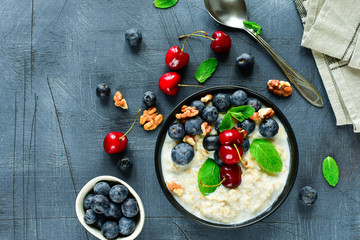 Oatmeal cereal porridge with fresh berries  in black bowl. Healthy breakfast. Top view on gray  table