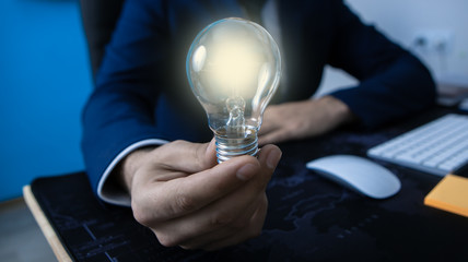 businessman in the office holds a shining lamp, the symbol of the idea; business concept