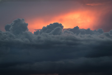 Growing cumulus clouds with the diffuse orange to red light of the setting sun as background