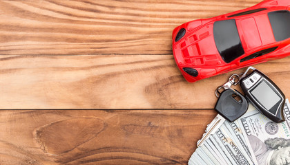  Red car toy with car key and money on wooden table. Top view. Space for text.
