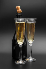 Two glasses of champagne with bottle of champagne on black.