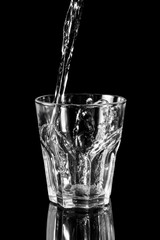 Water pouring into the glass on black reflective background.