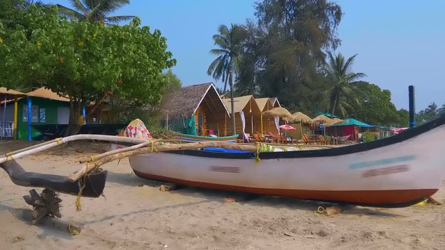 Wooden fishing boats with a net stand on the sand of the beach against the backdrop of palm trees, Goa, India. Shot in motion