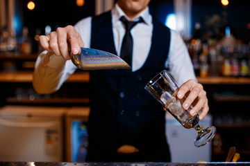 The bartender prepares a fresh, cold, alcoholic cocktail. Bar employee puts ice in his glass